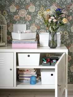 a white cabinet with drawers and flowers on the wall next to a birdcage