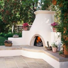 an outdoor fireplace surrounded by greenery and potted plants on either side of it