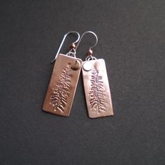 Majestic Tamarack pines are silhouetted against the glow of raw copper in these rustic and beautiful earrings. They are handcrafted from recycled copper and hang from sterling silver ear wires.  Measurements: Drop Length: 30mm (1 1/8in) Entire Earring Length: 45 mm (1 1/2in) Materials:  Copper  Copper is an element and a mineral known for its warm red-orange color, ductility, and malleability.  Copper has been used for thousands of years for jewelry and many people find that copper jewelry relie Etched Copper Jewelry, Rivet Jewelry, Pmc Jewelry, Etched Copper, Red Orange Color, Copper Cuff Bracelet, Basic Jewelry, Copper Cuff, Warm Red