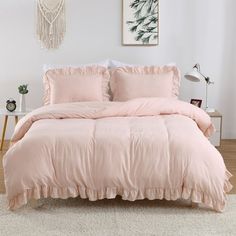 a bed with pink comforter and pillows in a white room next to a window