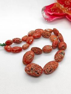 a long necklace with red beads and flowers on the side, next to it is a pink flower