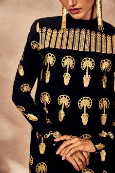 The black traveler's palm tunic set exudes elegance and sophistication with its foil printed tunic and intricate details. The a-line silhouette features a yoke adorned with gold sequin and dori embroidery, adding a touch of luxury. Full sleeves and a center back closure enhance its refined look. Paired with black straight pants featuring a side seam closure, this ensemble offers a polished and timeless style, perfect for any occasion where chic simplicity meets cultural richness. Gold Embroidered Palazzo Set For Festivals, Elegant Gold Palazzo Set With Embroidery, Elegant Gold Palazzo Set With Gold Embroidery, Traditional Embellished Black Palazzo Set, Black Embellished Palazzo Set For Evening, Evening Embellished Black Palazzo Set, Embellished Black Bollywood Palazzo Set, Evening Black Embellished Palazzo Set, Elegant Black Embellished Palazzo Set