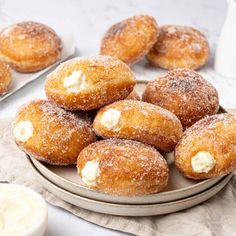 powdered sugar covered doughnuts on a plate next to a cup of cream