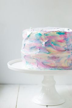 a white cake with colorful icing sitting on top of a white cake platter