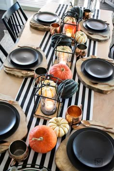 a table set with black plates and pumpkins