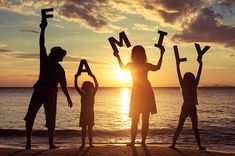 silhouettes of people holding up letters on the beach at sunset with the sun setting in the background