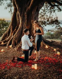 a man kneeling down next to a woman in front of a tree with candles on it