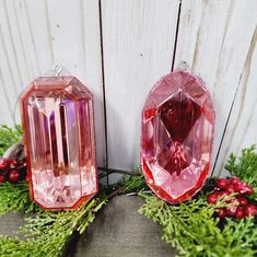 two pink glass ornaments sitting next to each other on top of a wooden table covered in greenery