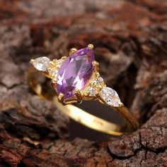 a yellow gold ring with an amethorate and white diamonds on it, sitting on a piece of wood