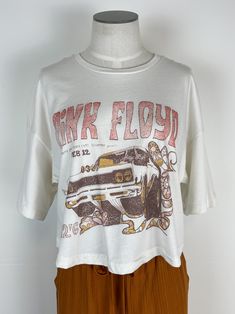 You'll love the iconic style of the Pink Floyd Essex Cropped Tee! This unique graphic tee is perfect for showing off your favorite classic rock band in an elevated, stylish way. It features a cropped length, off white color, and relaxed body and sleeves creating a timeless look that looks great with any outfit. Get ready to rock out in style! 100% Airlume Combed & Ringspun Cotton Officially Licensed MEASUREMENTS: LENGTH: S - 19.5" M - 20 3/8" L - 22" WIDTH: S - 20 1/4" M - 21 3/4" L - 23 3/4" Summer Band Merch Cropped T-shirt With Graphic Print, Summer Band Merch Cropped T-shirt With Crew Neck, Summer Band Merch Cropped T-shirt, Summer Band Merch Cropped T-shirt With Short Sleeves, Band Merch Cropped T-shirt For Summer, Casual Crop Top With Graphic Print For Concerts, Summer Band Merch Cropped T-shirt For Streetwear, Summer Band Merch Crew Neck Crop Top, Band Merch Graphic Print Crop Top For Concert