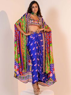 A three-piece Blue Indica Mirror Dhoti Skirt Set Paired with Bralette and Cape from the Juhi Bengani collection – Rang-Festive 2022. This gorgeous blue indica silk mirror dhoti skirt is paired with a heavy embroidered multicolored bralette blouse. The bright and vibrant colors with floral print, heavy embroidery of mirror, beads, stones, and thread sequence work enhance this satin dhoti skirt set. The indica blue dhoti skirt has a side opening at the waistline. This outfit is completed with a Dandiya Indowestern Outfit, Dhoti Skirt Outfits, Dhoti Skirt, Long Anarkali Gown, Organza Jacket, Cape Set, Ethnic Dresses, Kurta Patterns, Dream Wedding Decorations