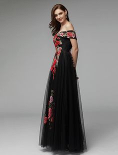 a woman in a long black dress with red flowers on the side and off shoulder