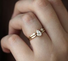 a woman's hand with two gold rings on top of her finger and the ring has three pear shaped diamonds