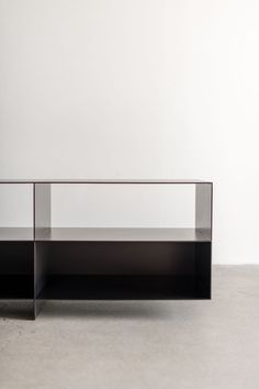 an empty glass shelf sitting on top of a cement floor in front of a white wall