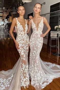 two women standing next to each other on a wooden floor wearing dresses with white flowers