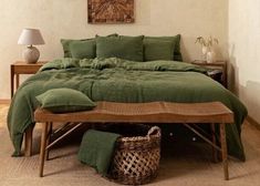 a bed with green linens and pillows in a white room next to a wooden table