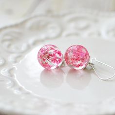 pink and white earrings with dandelions on them sitting on top of a table