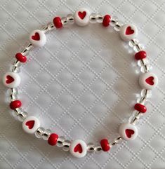 a red and white beaded bracelet with hearts on the clasp is sitting on a table