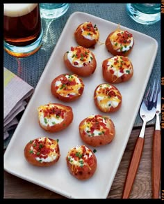 small baked potatoes with bacon and cheese on a white platter next to silverware