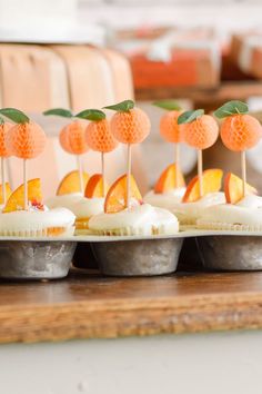 cupcakes with orange slices and green leaves on them are arranged in tin cups