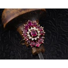 a ring with red stones and white diamonds on it sitting on top of a piece of wood