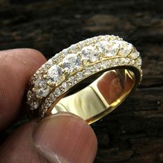 a hand holding a gold ring with white stones on the inside and outside, in front of a wooden surface