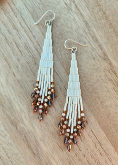 two pairs of white and brown beaded earrings sitting on top of a wooden table