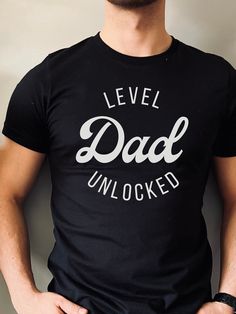 "The \"Dad Level Unlocked\" t-shirt is a fun and playful way for dads and soon-to-be dads to show off their fatherhood achievements. The text is a nod to the popular gaming culture phrase \"level unlocked,\" and highlights the new level of responsibility and joy that comes with becoming a dad. This t-shirt makes a great gift for Father's Day, birthday, or for a baby shower/baby announcement!  Bella + Canvas Brand Shirt ▶Unisex Adult Sizing ▶See Our Size Chart For Proper Sizing ▶For an oversized look, go 1-2 sizes up! ▶Rolled sleeves are for styling purposes only ▶Props used in photos are not included with the purchase ▶Please note that the colors of the design on the T-shirt may      appear slightly different due to variations in monitor settings. ✈ PROCESSING & SHIPPING ✈ Processing Time: Baby Announcements, Pregnancy T Shirts, Dad Pregnancy Announcement, Expectant Father, Baby Annoucement, Dad Tshirt, Father Shirts, Pregnancy Announcement Shirt