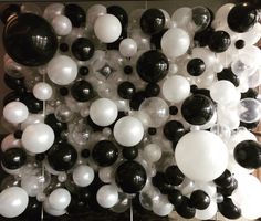 black and white balloons are hanging from the ceiling in front of a wall full of them