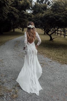 a woman in a white dress walking down a dirt road with trees and grass behind her