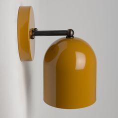 a yellow wall light hanging on the side of a white wall with a black handle