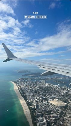 an airplane wing flying over the ocean and cityscape in miami, florida on a sunny day