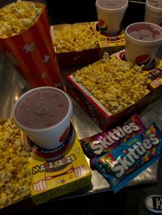 popcorn, drinks and snacks are on the table in front of some sodas at a movie theater