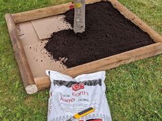 a wooden box filled with dirt next to a shovel and some gardening tools on the ground