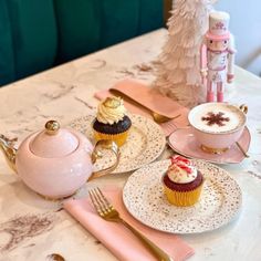 a table topped with plates and cups filled with cupcakes next to a tea pot