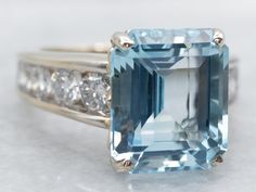 Adorn your finger with this stunning white gold ring featuring a mesmerizing emerald cut blue topaz. Channel set diamond shoulders add a touch of sparkle to this statement piece. Elevate your style with this unique and elegant ring. Metal: 14K White Gold Gem: Blue Topaz 7.37 Carats Gem Measurements: 9.9 x 11.8 mm, Emerald Cut Accents: 10 Diamonds totaling 1.06 Carats, SI in Clarity, G-H in Color Ring Size: 6 SKU #: A40118 Each piece has been identified and graded by a Graduate Gemologist who has been certified by the Gemological Institute of America (GIA). We have six brick-and-mortar storefronts in Maine, Massachusetts, and New Hampshire and have been in business for over 25 years! Please visit our Shop's About Page or our website for more information about our jewelry. For questions abou Channel Set Diamond Ring, Topaz And Diamond Ring, Womens Jewelry, Ring Blue, Ring Metal, Channel Set, Elegant Ring, Blue Topaz Ring, Color Ring