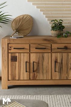 a wooden sideboard sitting on top of a rug next to a stair case and potted plant