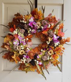 a wreath made out of leaves and flowers hangs on the front door to welcome guests