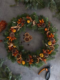 a wreath with oranges, pine cones and scissors on the table next to it