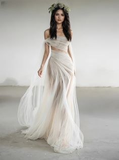 a woman wearing a white dress and veil with flowers on her head, standing in an empty room