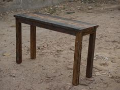 a wooden bench sitting on top of a dirt ground next to a building with no roof