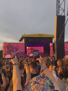 a group of people taking pictures with their cell phones at an outdoor music festival or concert