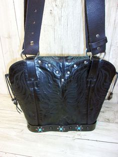 Infuse your look with a dose of Santa Fe style with this one-of-a-kind leather handbag. Hand-crafted from up-crafted cowboy boots and belts. Tote style with no pockets No two alike, signed and numbered Magnetic closure and metal concho detail Measures approximately 10"x12"x5" This exquisite leather bag is more than just a cowboy boot purse - it's a wearable work of art that celebrates the spirit of the American West. Perfect for the lady who wants to infuse her look with a dose of Southwestern s Festival Leather Bag With Belt Included, Leather Festival Bag With Belt Included, Western Leather Bags With Concho Details, Hand Tooled Leather Bags For Western-themed Events, Hand-tooled Leather Bags For Western-themed Events, Western Style Bags For Festivals, Western Leather Bags For Rodeo, Bohemian Leather Bag With Concho, Hand Tooled Leather Bags For Rodeo