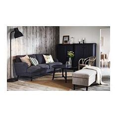 a living room with wood paneling and grey couches, coffee table, lamp and rug