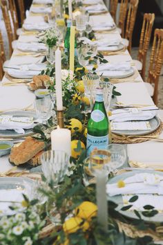 a long table is set with yellow and white flowers, candles, and place settings