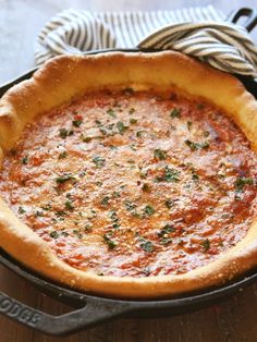 a deep dish pizza in a cast iron skillet on a wooden table with a striped napkin