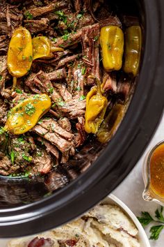 a crock pot filled with beef and peppers next to some bread on the side