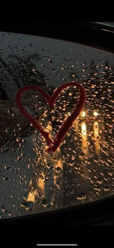 a heart drawn on the windshield of a car in the rain with candles behind it