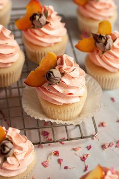 cupcakes with pink frosting and peaches on top are sitting on a cooling rack