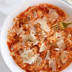 a white bowl filled with sauce and cheese on top of a table next to a fork